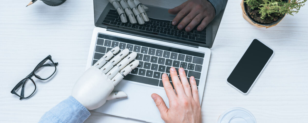 cropped image of businessman with prosthetic arm using laptop at table with eyeglasses, smartphone