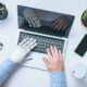 cropped image of businessman with prosthetic arm using laptop at table with eyeglasses, smartphone