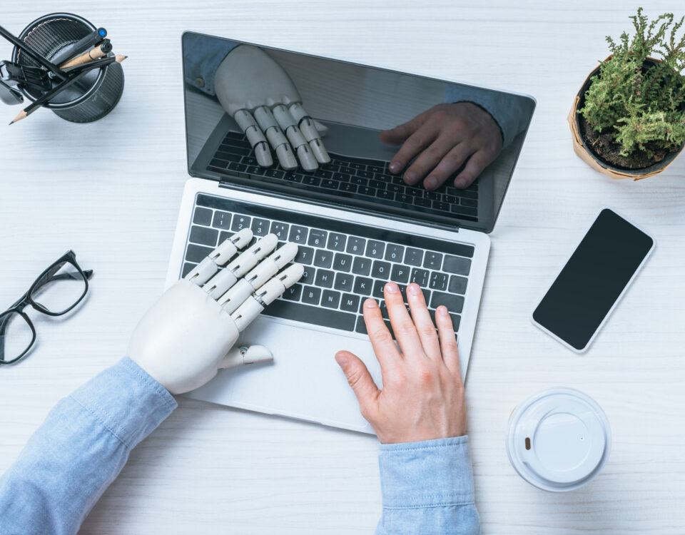 cropped image of businessman with prosthetic arm using laptop at table with eyeglasses, smartphone